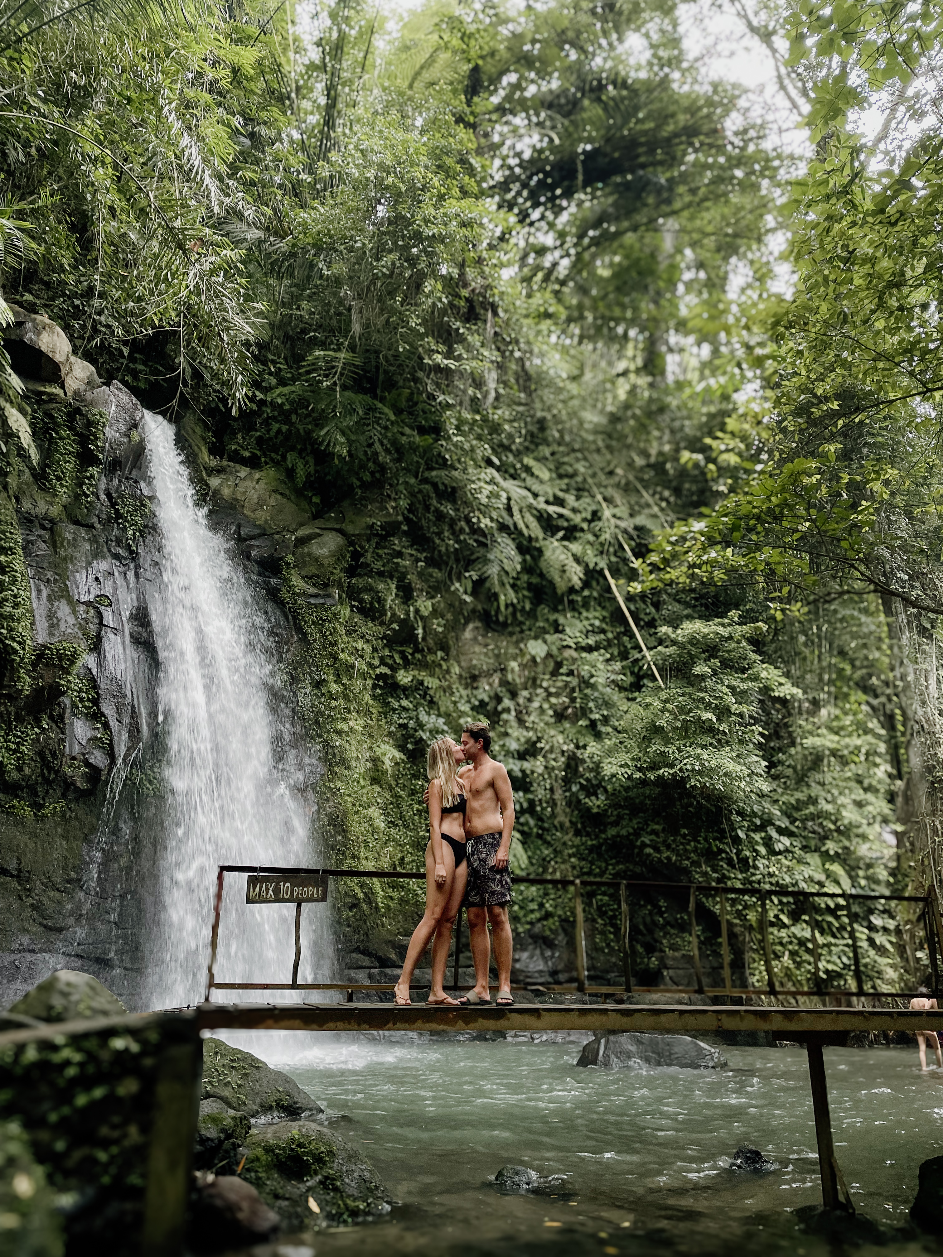 Couple on bridge at Ulupetanu Waterfall surrounded by lush greenery